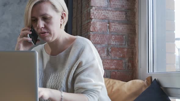 Adult European Bondin in a Cafe Works Online in a Laptop and Talks on the Phone