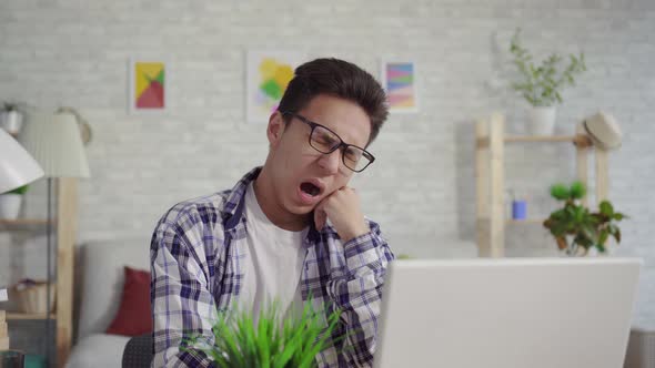 Sleepy Young Asian Man in a Shirt Sitting at the Laptop