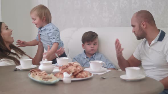 Young Mum Playing with Her Baby Boy While Dad Talking To His Son Sitting at the Tea Table