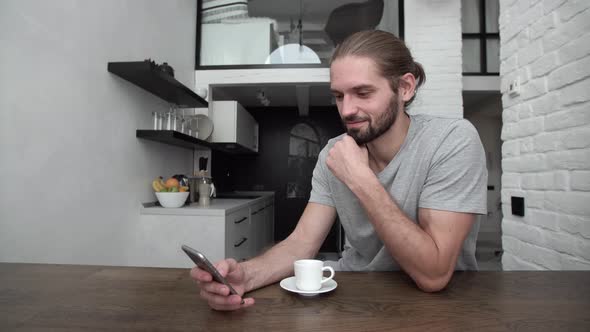 Man With Mobile Phone Drinking Coffee At Home Kitchen