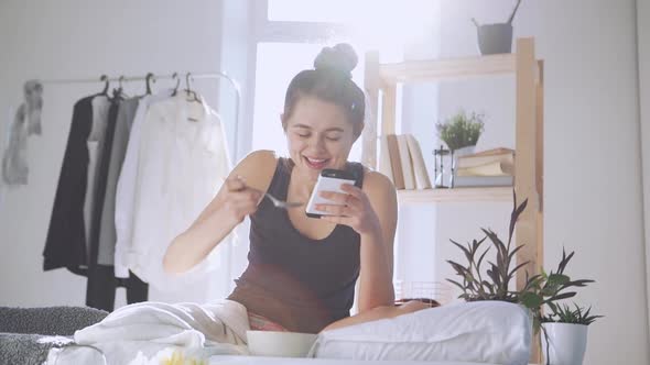 Young Caucasian Female Eating Breakfast and Chatting with Boyfriend Using Smartphone in Slowmotion