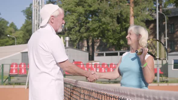 Adult Woman Shakes Hands with Handsome Mature Man Rival Standing on a Tennis Court