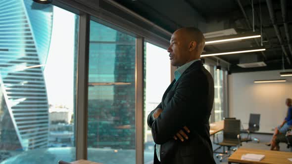 Aframerican Entrepreneur Standing Near Huge Modern Office Window with Serious Expression