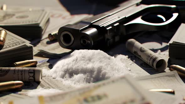 Ammo bullets and a gun on a table covered with countless dollar bills and drugs