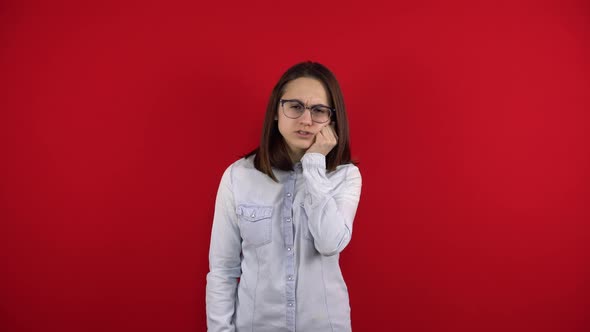 A Young Woman Wearing Glasses Has a Toothache and Touches Her Cheek with Her Hand