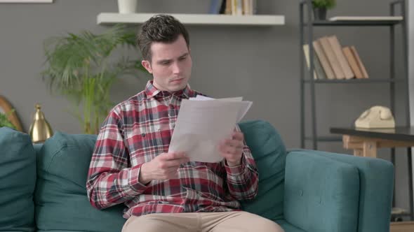 Man Reacting to Loss on Documents Sofa