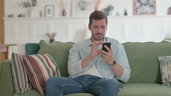 Young Man Using Smartphone on Sofa
