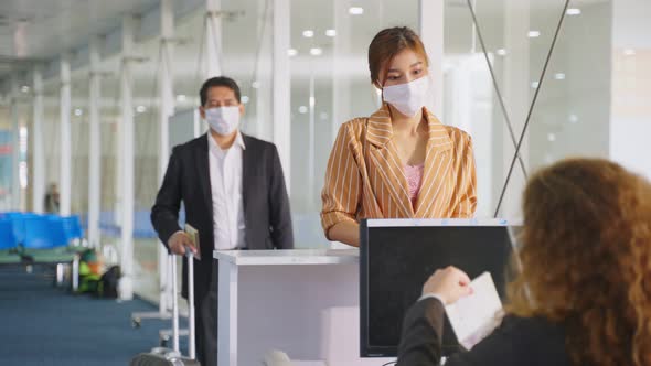Travelers passengers wearing mask, give passport to female officer at airline check in counter.