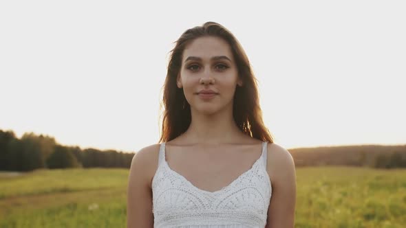 Woman in a Good Mood Standing in Field on Summer Evening. She Looks Into Camera and Smiles