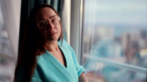 Charming Middle Aged Woman with Glasses is Looking at Window in Morning Time Resting at Home