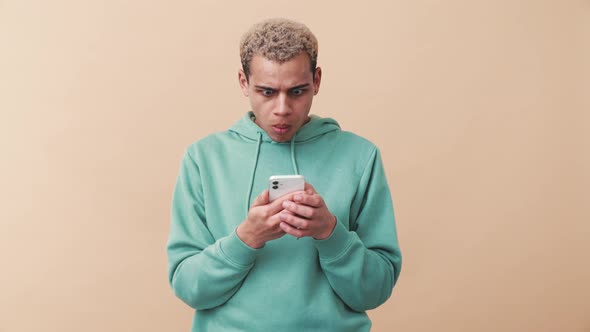 Pretty curly-haired man wearing blue hoodie emotionally looks at the phone