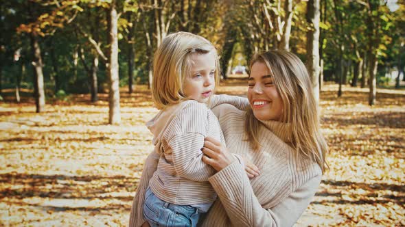 Young Mom is Smiling Holding Little Daughter in Arms and Tickling Her During Their Walk in Autumn
