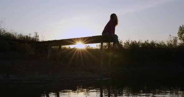 Beautiful Girl Contemplates the Lake Sitting on the Pier