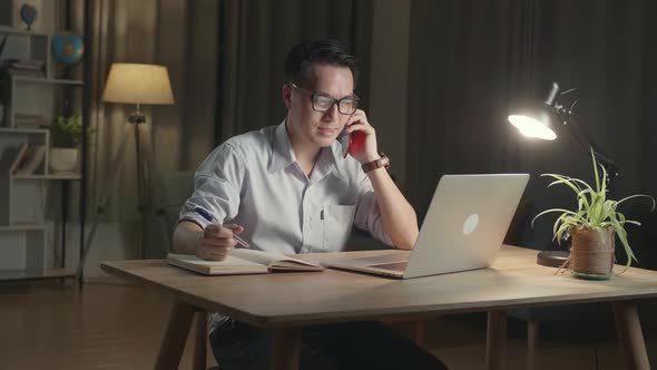 Businessman With Laptop Computer Calling On Smartphone From Home At Night