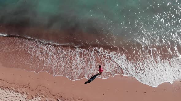 Woman walking along sandy beach with waves splashing. Aerial Top view. Tropical nature concept