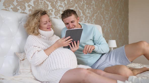 Pregnancy, Parenthood And Technology Concept - Pregnant Couple Using Tablet