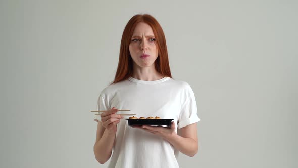 Portrait of Dissatisfied Young Woman Eating Unappetizing Sushi Rolls with Chopsticks Dissatisfied