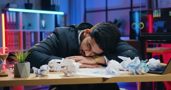 Businessman which Sleeping on the Table with Computer and Crumpled Papers in the Office at Late Time