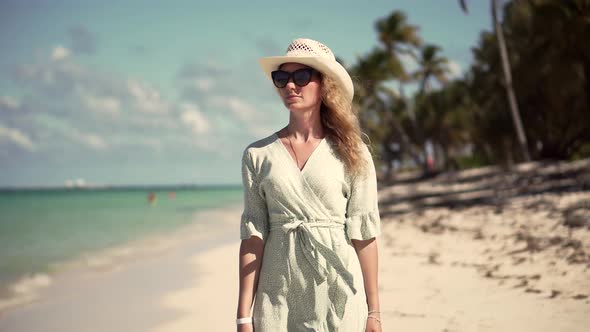 Woman Relaxing On Bahamas Flowing Dress Blowing In Wind. Woman In Hat Walks Along Beach On Caribbean