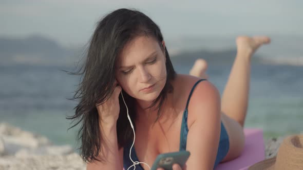 Girl Wears Earphones While Lying on the Beach in a Beautiful Sea Landscape