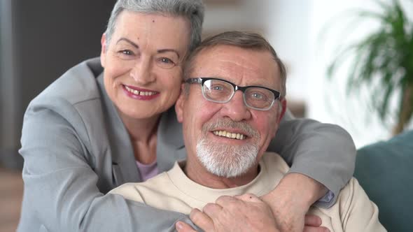 Man and a Woman Hugging and Looking at the Camera While Sitting on the Sofa