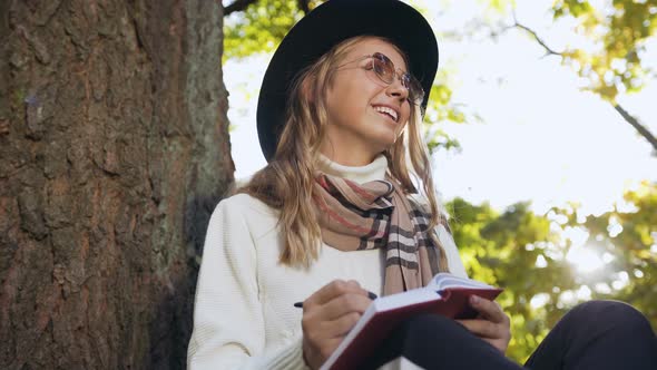 Young Woman in Stylish Hat Writing Something in Notebook