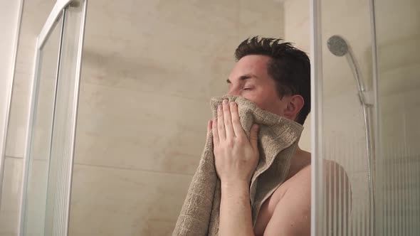 Portrait of a Young Man Who Wipes His Face with a Bath Towel in the Bathroom