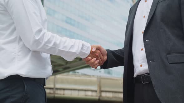 Close up of Asian businessmen making handshake in the city with highrise building in background.