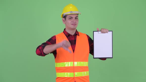 Stressed Young Multi Ethnic Man Construction Worker Showing Clipboard and Giving Thumbs Down