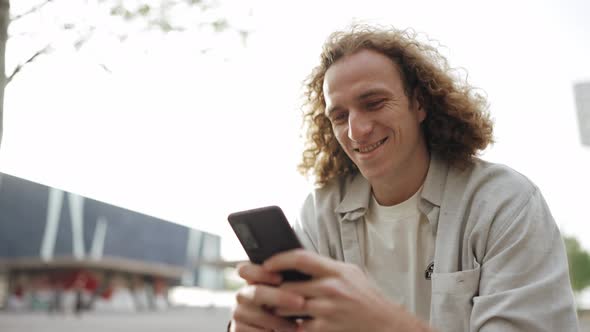 Cheerful curly-haired man texting by mobile