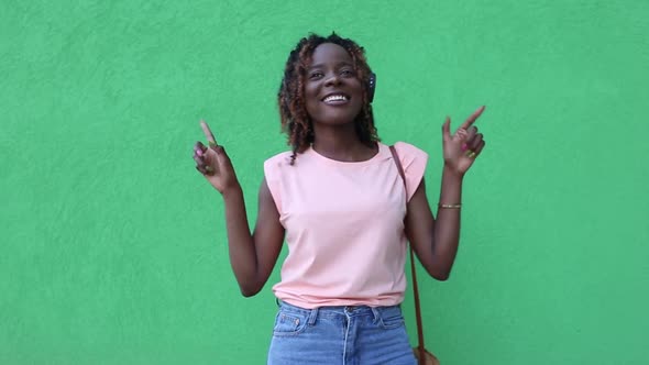 African-American woman listens to music with headphones and dances, on a green background