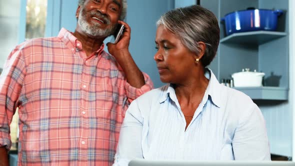 Senior couple using mobile phone and laptop in kitchen