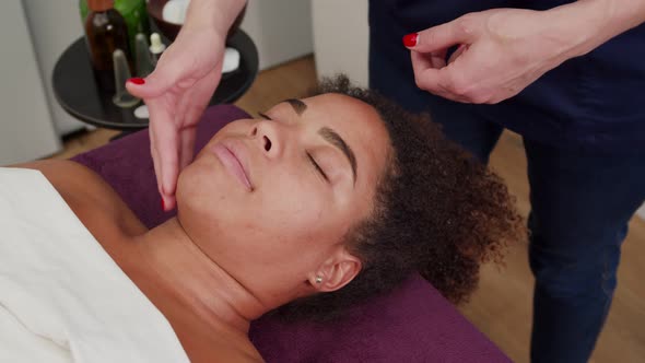 Skilled Cosmetologist Doing Facial Massage with Gua Sha Stone Indoors