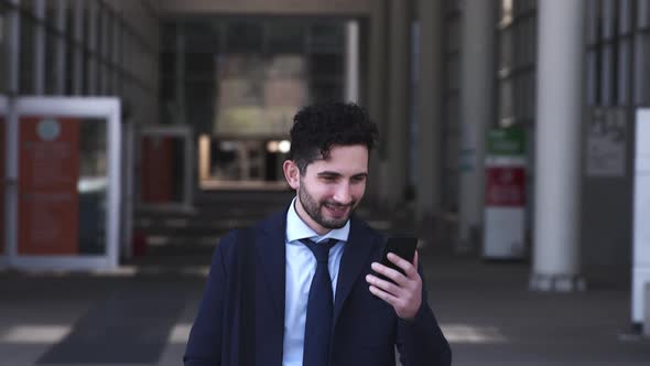 Smiling businessman walking in city, looking at smartphone