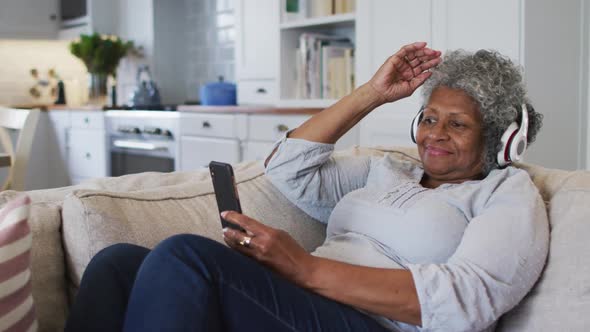 Senior african american woman wearing headphones having a video call on smartphone at home