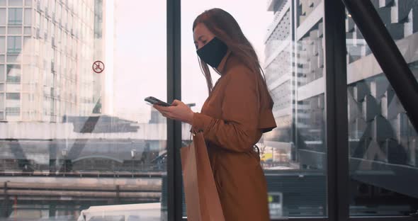 Side View Young Beautiful Business Woman in Face Mask Walks Using Mobile Office App at Mall Window