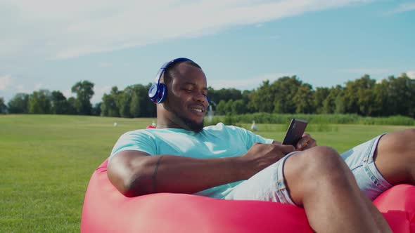 Black Man in Headphones Resting on Air Sofa Outdoors