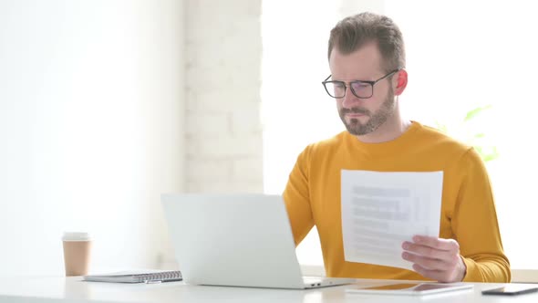 Man with Laptop Having Loss While Reading Documents