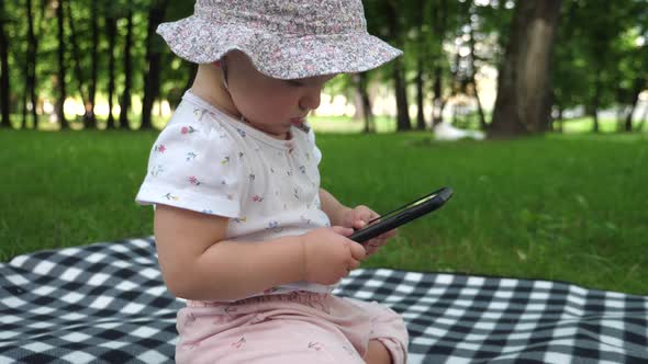 Baby Girl on the Picnic Blanket Concentrating on Her Phone at the Park. Babies and Technology