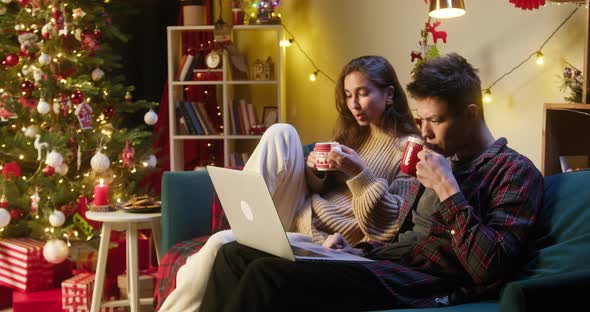 Young Couple Watching Film on Laptop Sitting on Sofa in Living Room