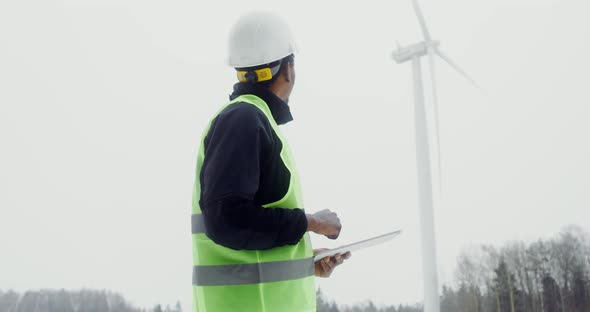 A Man in a Work Uniform is Diagnosing a Wind Turbine Using a Digital Tablet