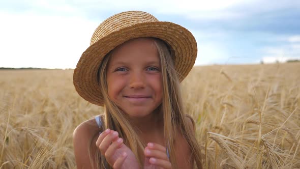 Beautiful Smiling Girl in Straw Hat Looking Into Camera Against the Background of Barley Field at