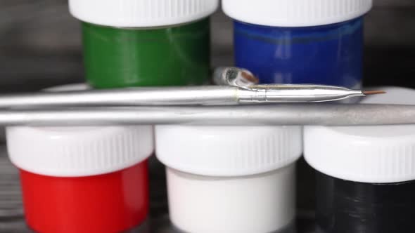 A Set Of Gouache And Brushes. Jars Of Paint Stand In A Pyramid.  Slider Camera. On Pine Boards. alt