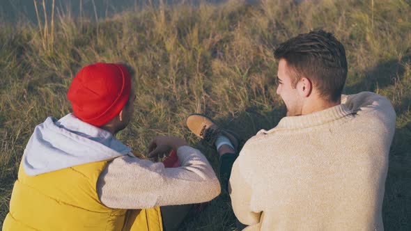 Happy Men Talk Sitting on Dry Grass at Campsite in Evening