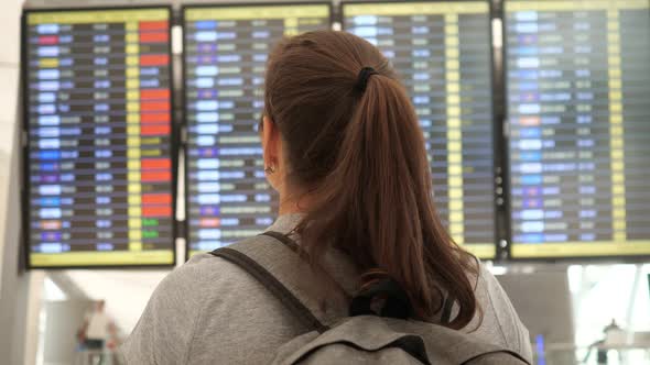 Woman with Ponytail Examines Flight Schedule in Airport