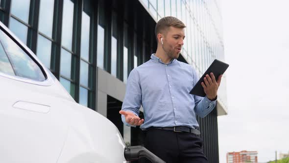 Young Handsome European Man with Wireless Headphones Speaking on a Video Chat on His Tablet Near His