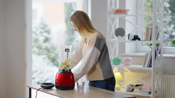 Side View of Slim Attractive Young Woman Putting Chopped Fruits in Blender