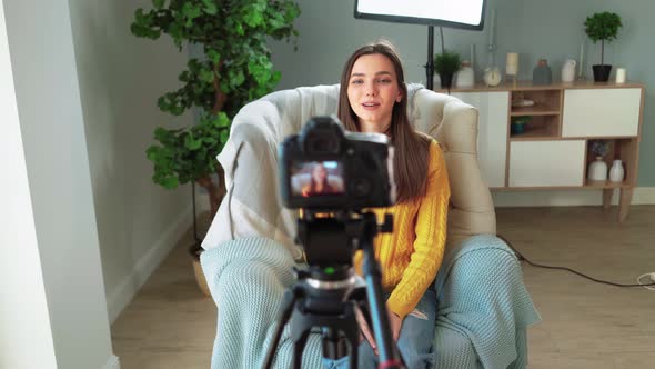 Beautiful Girl Blogger in Yellow Sweater is Filming Her Blog on Camera at Home