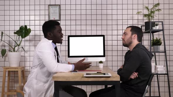 Doctor Showing Medical Records on His Computer To His Patient, He Is Pointing at the Screen