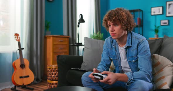 Teenager Boy Playing Game with Joystick Enjoying Sitting on Sofa in Living Room at Home